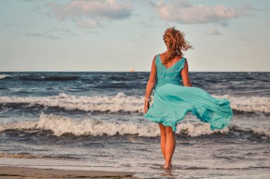 Kumsaldaki güzel sarışın kadın. Polonya sahilinde mavi elbiseli bir kız..