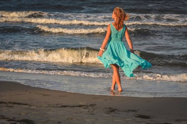 Kumsaldaki güzel sarışın kadın. Polonya sahilinde mavi elbiseli bir kız..