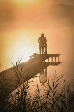 Göl kenarında güzel bir sabah sahnesi. Baba ve oğul güneşin doğuşunda balık tutuyor..