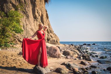 Yaratıcı tatil deniz kenarı seansı. Sahilde zarif kırmızı elbisesiyle güzel bir kadın. Kendi konseptiniz veya metniniz için alanı olan çerçeve.