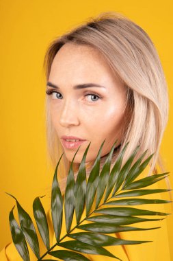 Sarı elbiseli, güzel sarışın bir kadının güzel portresi. Sarı arka planda yeşil bir yaprak tutuyor.