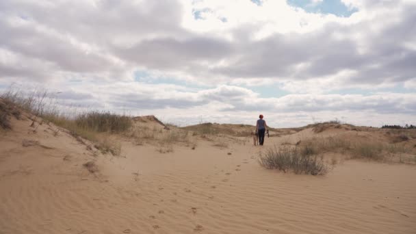 Kobieta wędrowca z psem spacerującym po piaszczystych wydmach pustyni — Wideo stockowe