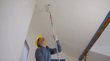 Bir adam silindirle duvar boyuyor, tavan arası zeminini onarıyor.