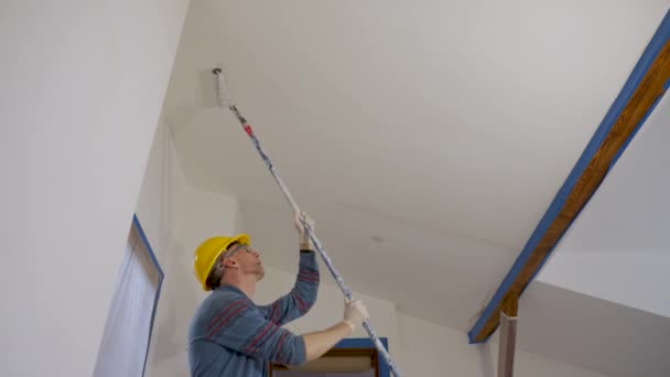 A man paints a wall with a roller, makes repairs in the room of the attic floor — Αρχείο Βίντεο