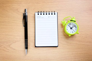 Ofis kalemli yeşil çalar saat ve ahşap bir masanın üzerinde boş defter.