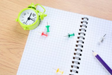 Masadaki renkli kalem, klipsler ve çalar saatle defteri kapat