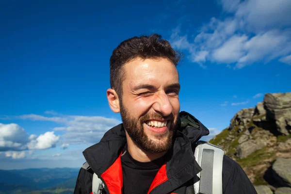 Göz kırpan, yürüyüş kıyafetleri içinde neşeli bir adamın portresi.