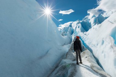 Bir kadın Perito Moreno Buzulu 'nda karlı duvarların arasında duruyor ve sağa bakıyor.