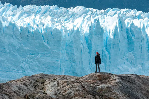 Egy nő áll a sziklafalon a Perito Moreno gleccser mellett, és jobbra néz. — Stock Fotó