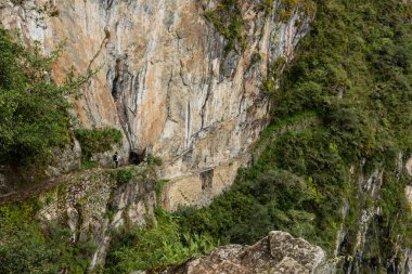 Dişi bir turist dar bir yolda yürüyor dağdaki küçük bir kapıya doğru, Machu Picchu, Peru