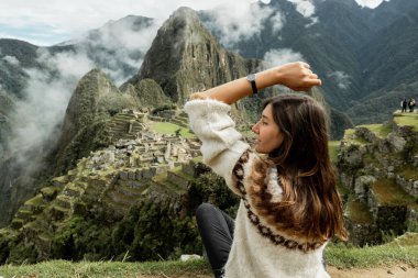 A profile portrait of a young woman with the background of Machu Picchu