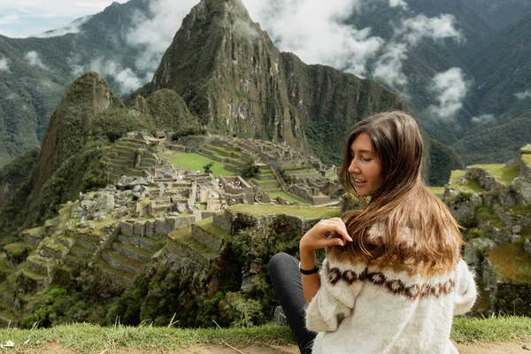A beautiful young tourist sitting on a the edge of the hill with a stunning view on Machu Picchu — Stockfoto