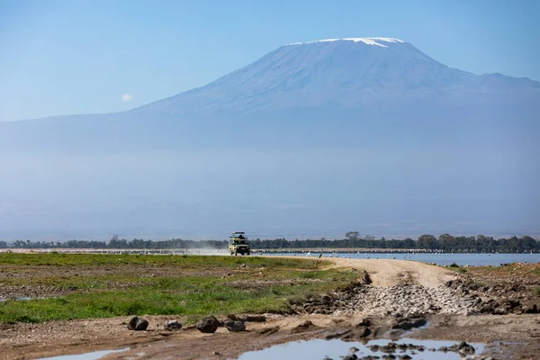 PARQUE NACIONAL AMBOSELI, KENIA - 17 DE SEPTIEMBRE DE 2018: Un jeep se mueve en la carretera junto al lago con el Monte Kilimanjaro al fondo — Foto de Stock