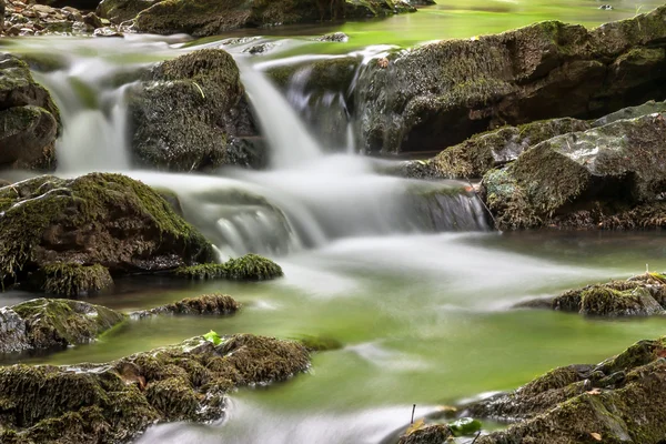 Seidiges Wasser, das über grüne, moosbewachsene Flächen fällt — Stockfoto