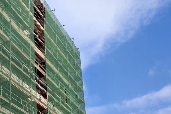 Escalera y andamios en un sitio de construcción, cubiertos con malla en el fondo del cielo . — Foto de Stock