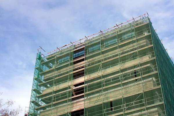 Escalera y andamios en un sitio de construcción, cubiertos con malla en el fondo del cielo . — Foto de Stock