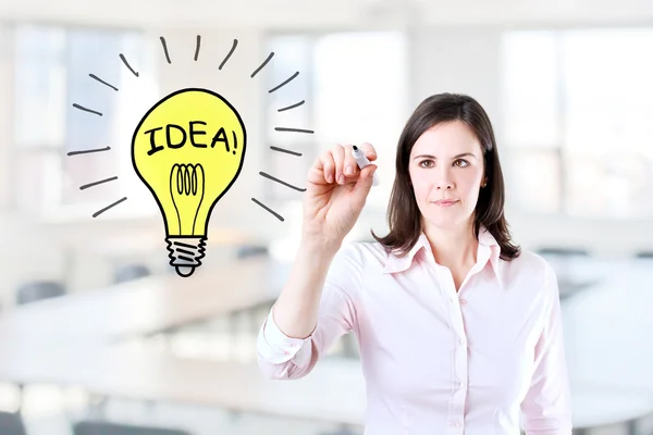 Young business woman drawing a light bulb. Office background. — Stock Photo, Image