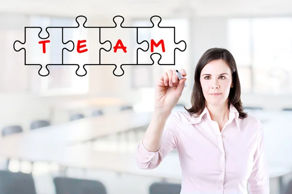 Businesswoman drawing a Teamwork Puzzle Concept on the virtual screen. Office background. — Stock Photo, Image