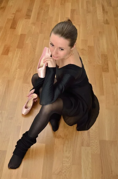 Ballerina in Schwarz auf dem Boden sitzend mit Ballettspitzschuhen in den Händen — Stockfoto