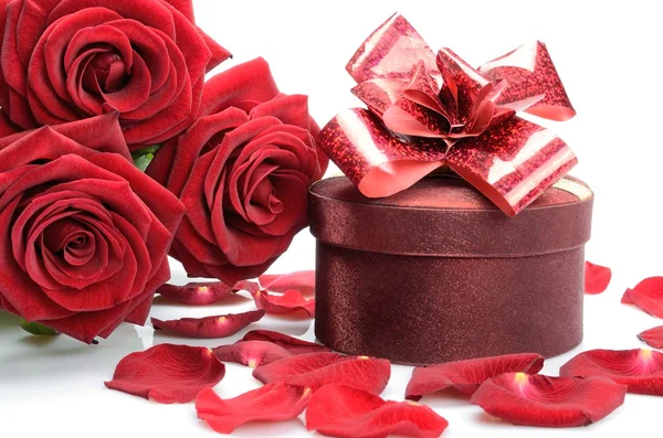 Geschenkbox, Blütenblätter und ein Strauß roter Rosen — Stockfoto