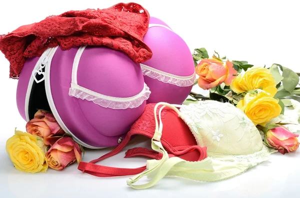 Vrouwelijke kleine koffer voor het opslaan van lingerie en roze bloemen in stilleven Stockafbeelding