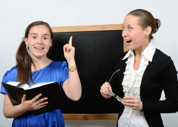 Pedagoog vrouw en een schoolmeisje in de buurt van blackboard studeren met een boek — Stockfoto