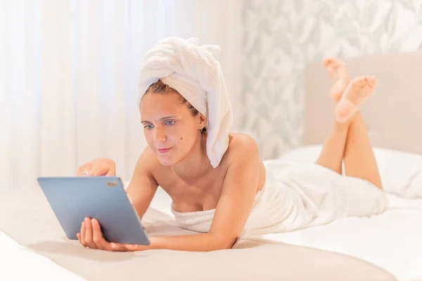 Dorosła kobieta owinięta w ręczniki przy użyciu tabletu cyfrowego. — Zdjęcie stockowe