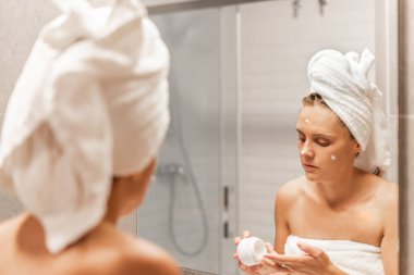 Yetişkin bir kadın elinde kremayla nemlendirici sürüyor..