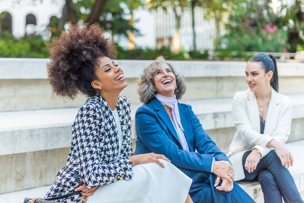women seated with their legs crossed and dressed in suits