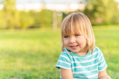 A little boy smiling sitting on grass in a park