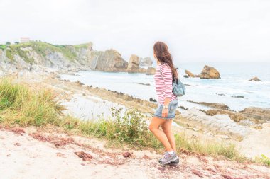 Kayalık sahilde yürüyen isimsiz kadın turist.