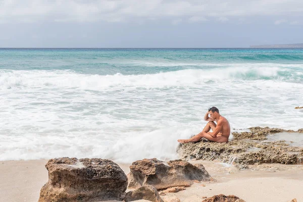 Γυμνό αρσενικό κάθεται σε βράχια κοντά στη θάλασσα — Φωτογραφία Αρχείου