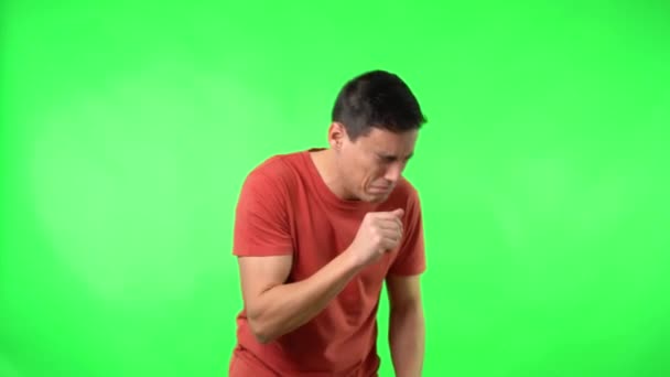 Hombre tosiendo con el puño cerca de la boca mientras está de pie contra chromakey — Vídeo de stock