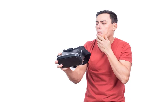 Puzzled man looking at VR goggles in studio —  Fotos de Stock