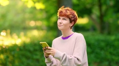 İkili olmayan kişi, gülümseyen ve düşünceli bir yüz ifadesi olan bir cep telefonuyla mesaj gönderiyor.