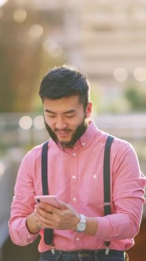 Şık Asyalı adam şehirde cep telefonunu kullanırken eliyle işaret ediyor.