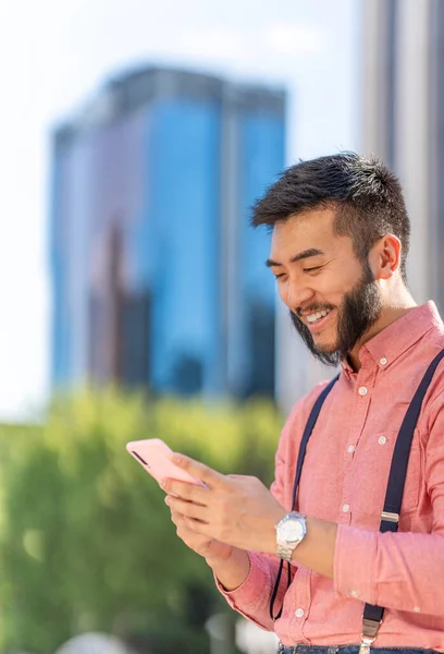 Asian businessman in shirt and braces smiling while using a mobile with a cityscape in the background