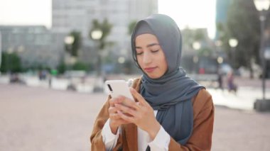 Meydanda cep telefonuyla mesaj gönderirken gülümseyen Müslüman kadın