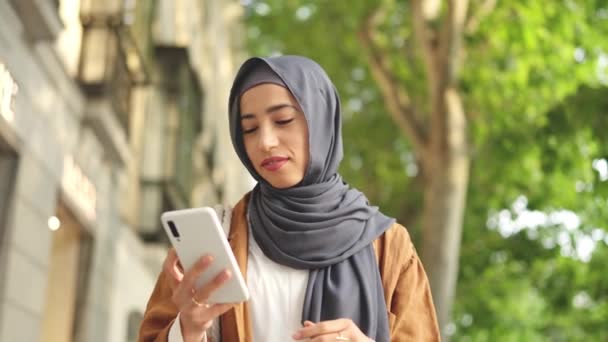 Mujer Musulmana Feliz Sonriendo Mientras Camina Usando Móvil Calle — Vídeo de stock