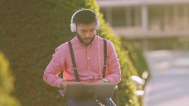 Parkta kulaklık kullanırken uzaktan kumandalı bir bilgisayarla çalışan Asyalı bir adam.