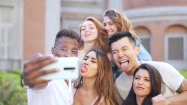 Dışarıda selfie çekerken şaka yapan ve yüzünü buruşturan çok ırklı bir arkadaş grubu.