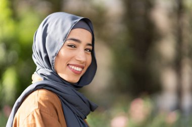 Parktaki kameraya gülümseyen tesettürlü güzel müslüman bir kadının portresi.