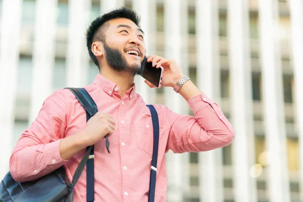 Smiling asian man carrying a bag while talking to the mobile in the street in the city