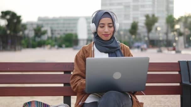笑顔のイスラム教徒の女性でヒジャーブ州の作業でリモートでノートパソコンが正方形に座って — ストック動画