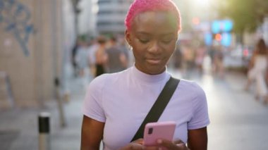 Güzel, modern, pembe saçlı Afrikalı bir kadın sokakta gülümserken bir mesaj yolluyor.