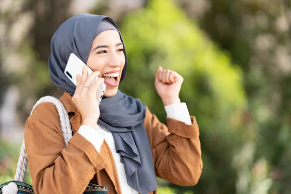 Mulher Muçulmana Levanta Punho Para Comemorar Enquanto Conversa Com Celular — Fotografia de Stock