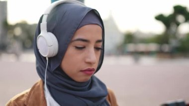 Muslim woman in hijab working with a laptop sitting on a bench in a city square