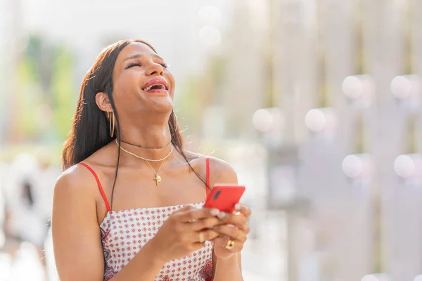Portrait with copy space of a trans woman laughing while using the mobile in the street