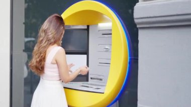 Young woman in white dress withdrawing money from the ATM in the street