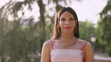 Parkta gülümseyen trans kadın başparmağını kaldırıyor.